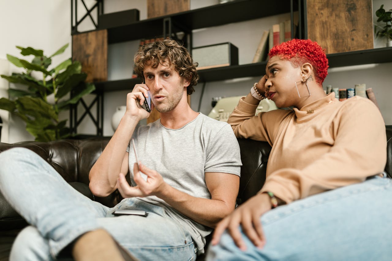 Two friends share a serious moment during a phone call on a cozy couch.
